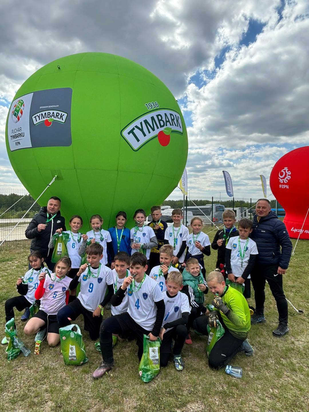 młodzi sportowcy pozujący do zdjęcia pod balonem na łące 