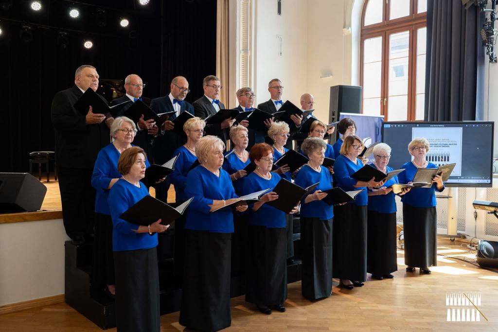 Osoby w strojach chóralnych stojące w pomieszczeniu i śpiewające