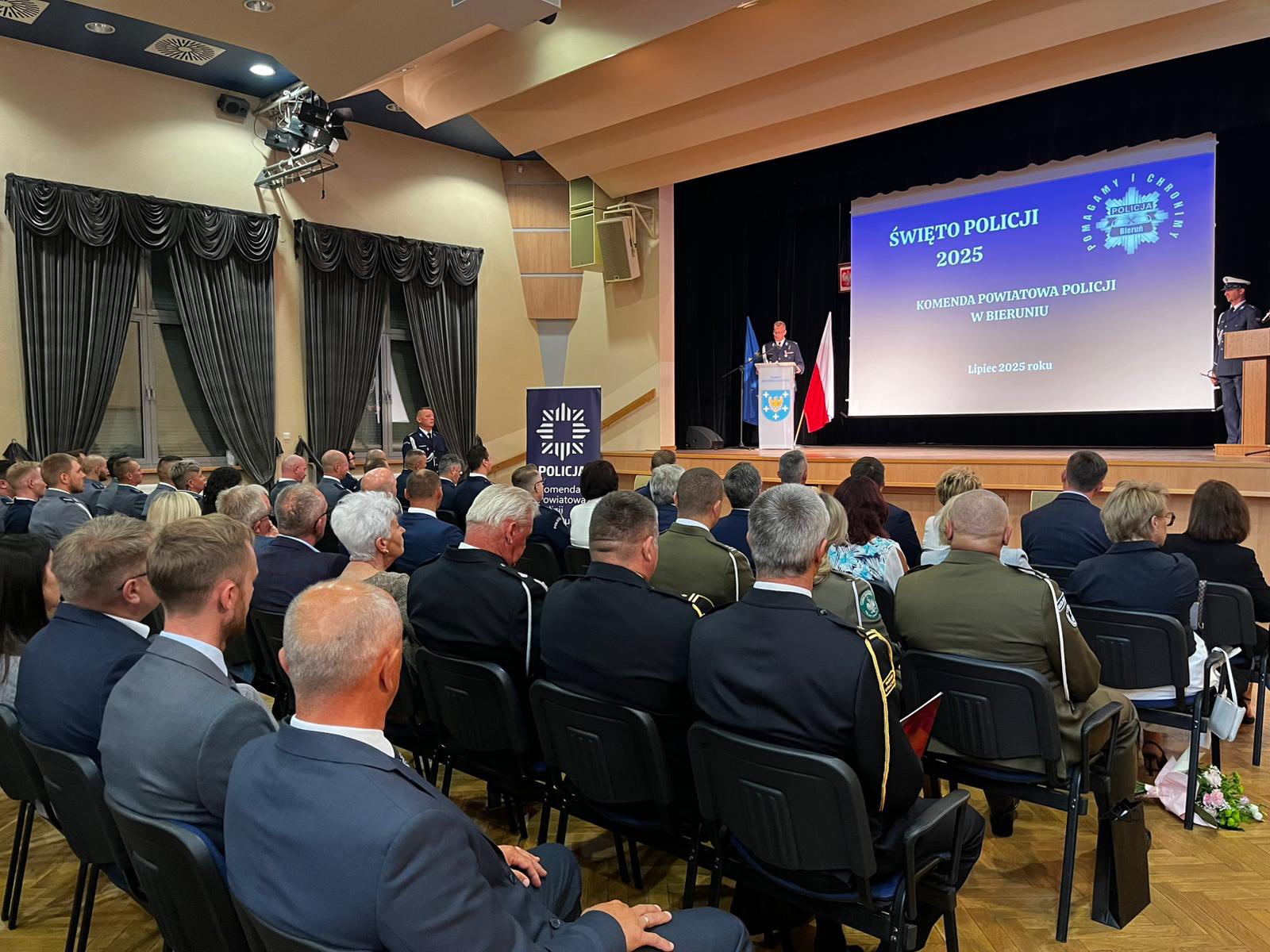 Osoby siedzące na sali w układzie teatralnym.