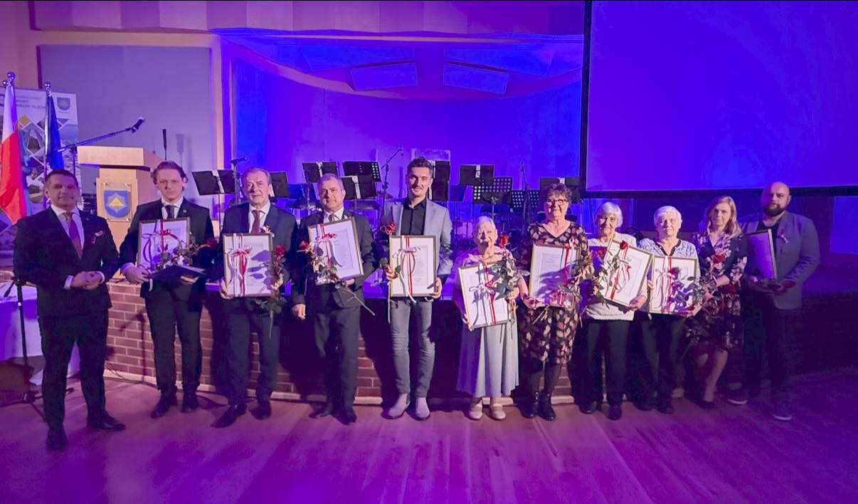 Osoby pozujące do zdjęcia przed sceną na sali 