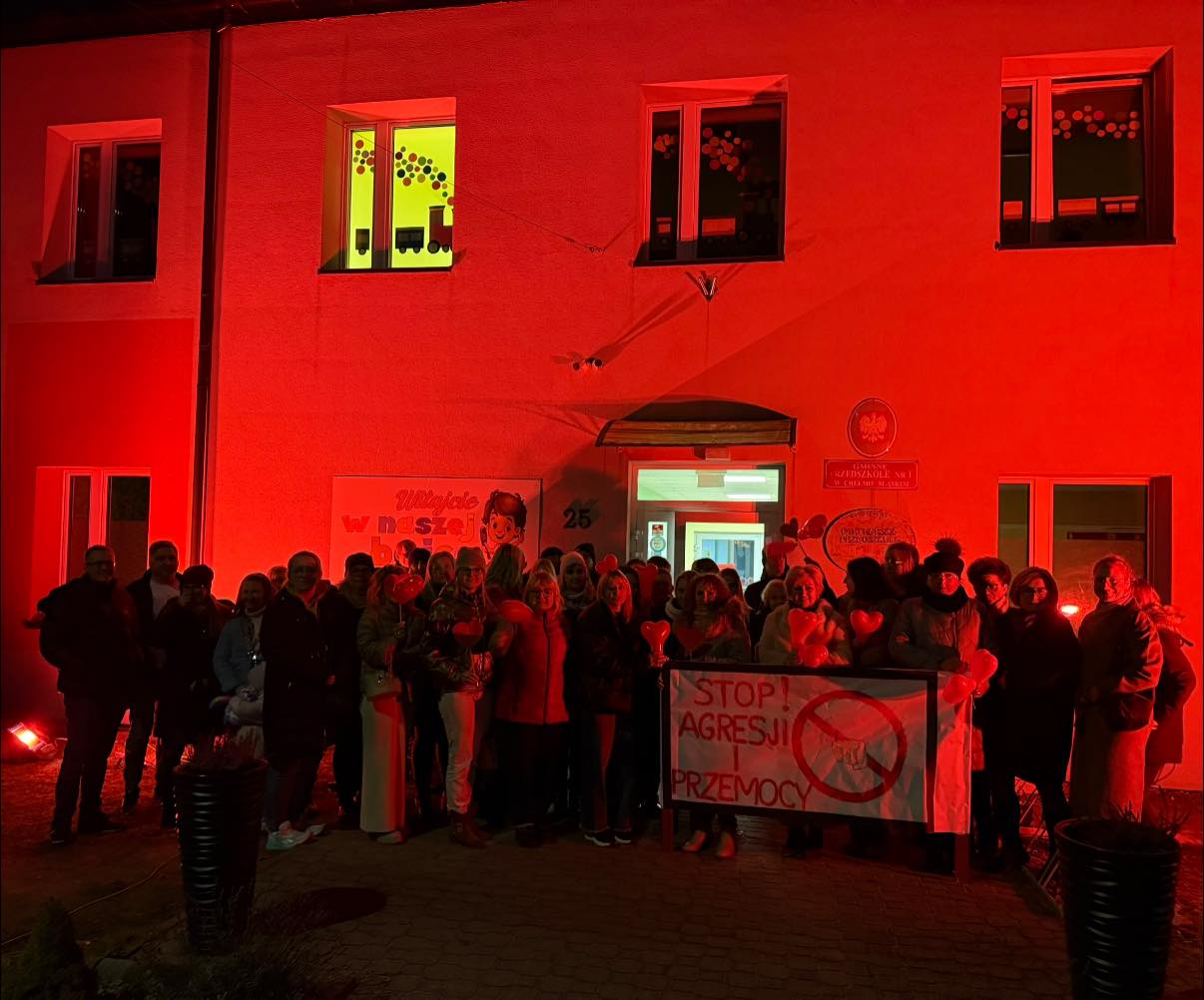 Przedszkole - budynek podświetlony na czerwono i stojące przed nim osoby z transparentem 