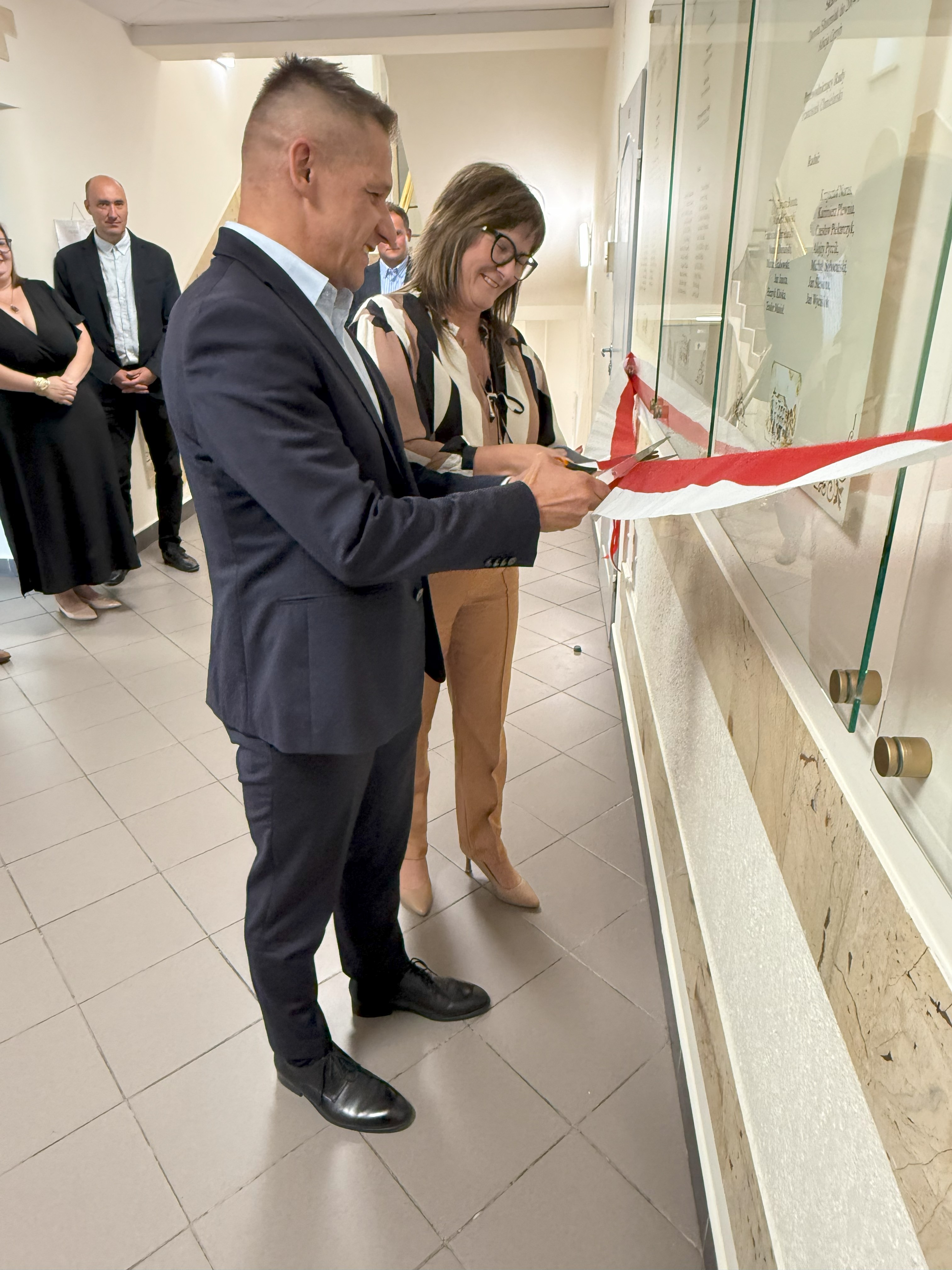 Mężczyzna i kobieta przecinają biało - czerwoną wstęgę