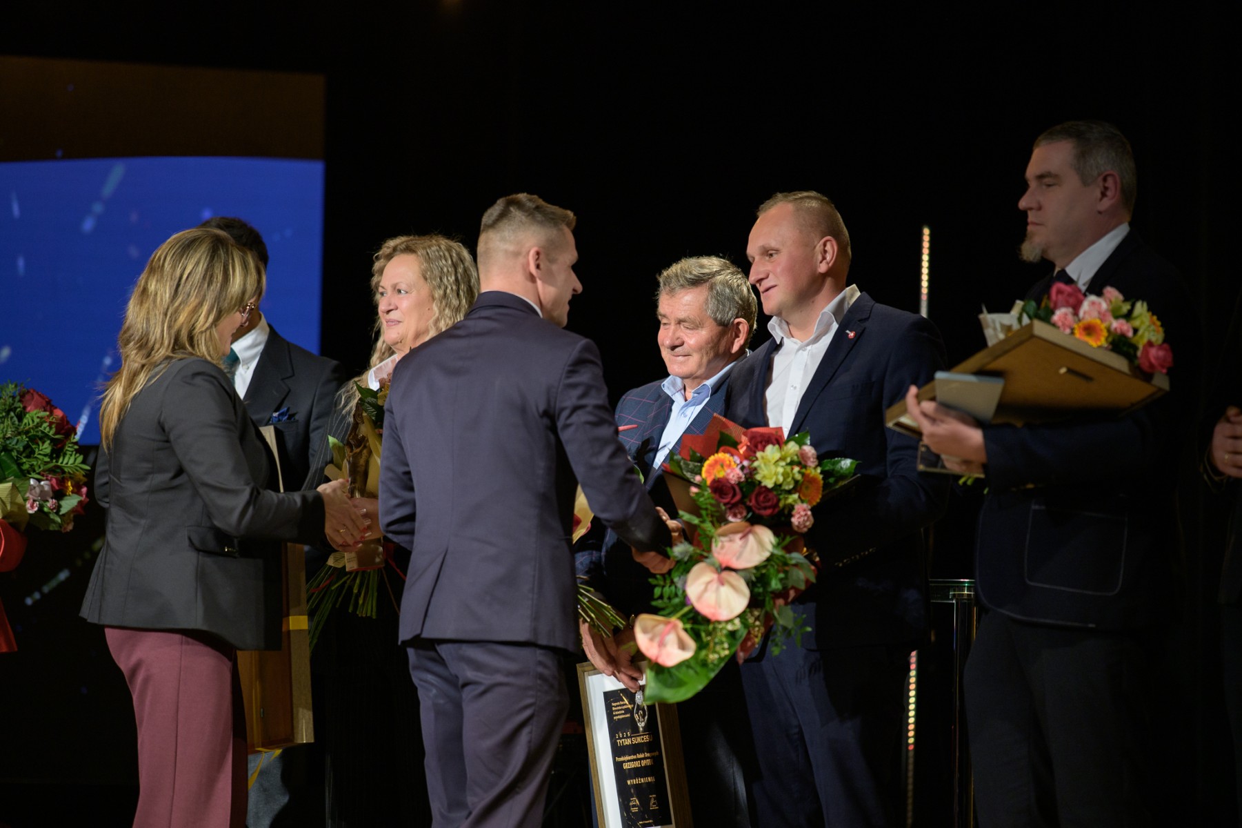 Osoby stojące na scenie gratulujące sobie. 